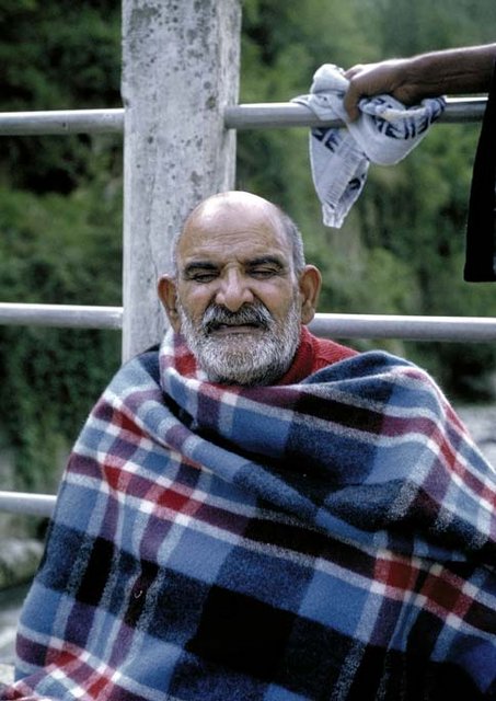 Neem Karoli Baba seated outdoors, wrapped in a checked blanket